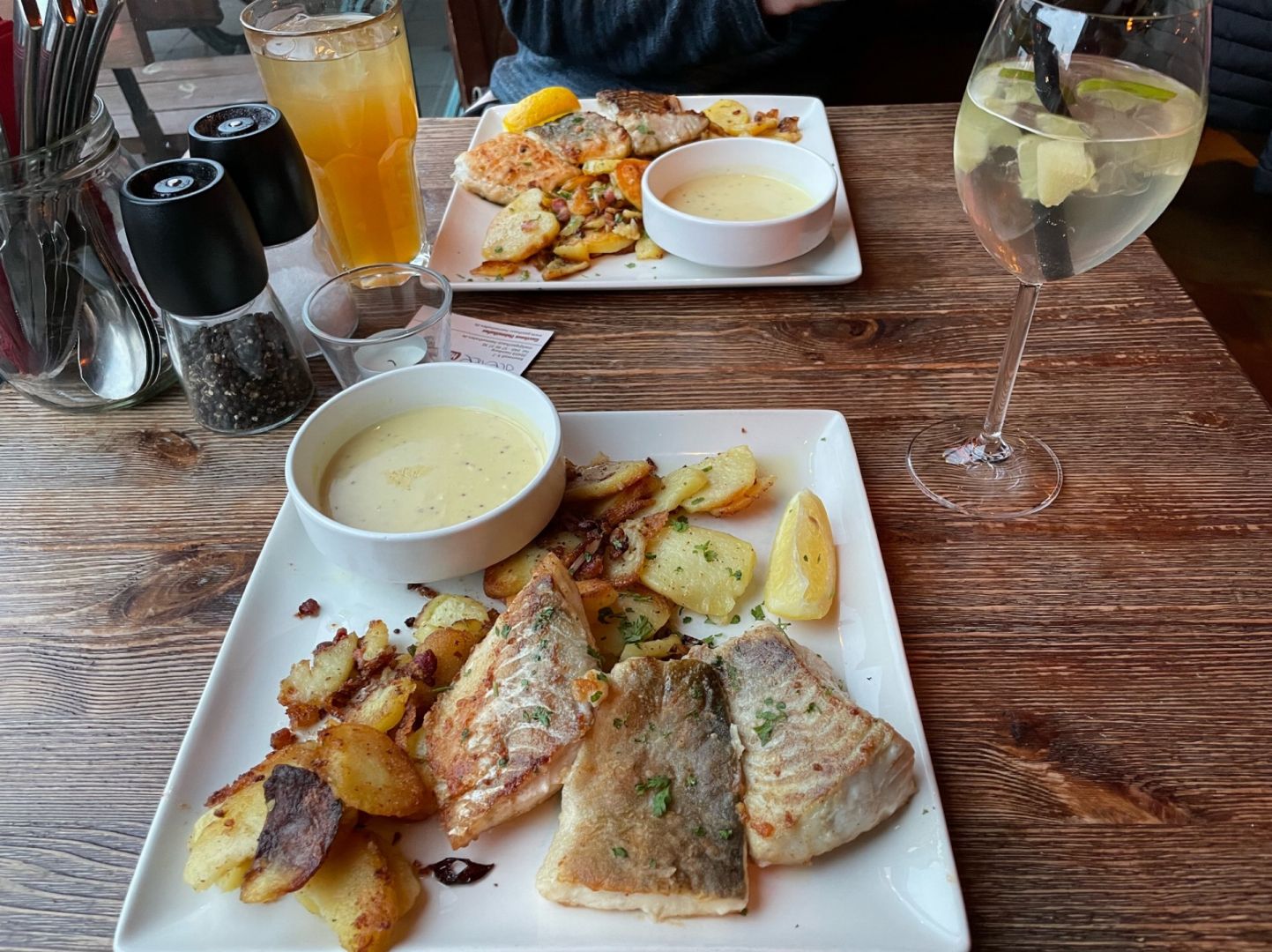 zweimal Pannfisch mit Bratkartoffeln und Senfsoße auf weißen rechteckigen Tellern und Holztisch